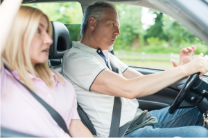 Man gripping the steering wheel tightly while driving, with a concerned passenger beside him.