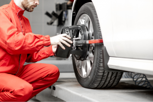 Mechanic in red uniform performing a tire alignment check on a vehicle using specialized equipment.